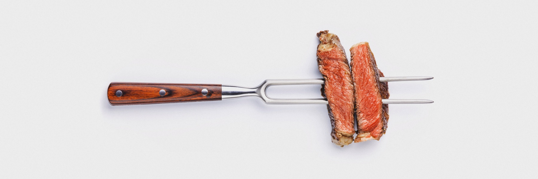 Slices of Medium rare grilled Steak Ribeye on meat fork.